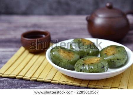 A plate of Qingtuan stuffed with egg yolk and dried meat floss, a cup tea and a teapot on wooden table. Traditional seasonal Chinese delicacies in Jiangnan area around the time of Tomb Sweeping Day.  Royalty-Free Stock Photo #2283810567