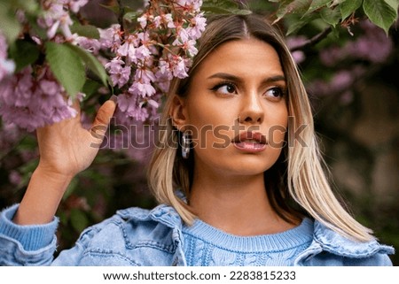 Amazing spring beauty portrait of young blonde girl posing next to blooming tree.