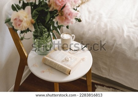 Still life details in home interior of living room. Open book with glasses, cup coffee and bouquet white pink peonies flowers. Read and rest. Cozy home Royalty-Free Stock Photo #2283816813