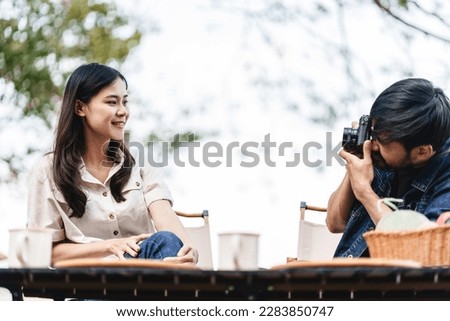 Asian man takes picture of girlfriend.
Happy Asian couple taking photo by camera in camping outdoors in nature