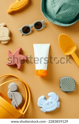 Baby sunscreen lotion tube with beach toys on color background. Flat lay, top view