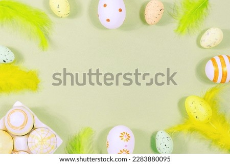 Top view of Easter eggs painted in different patterns and feathers on a green background. Copy space. Place for an inscription
