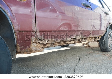 Horizontal photo of rusty thresholds and doors of a red car close-up