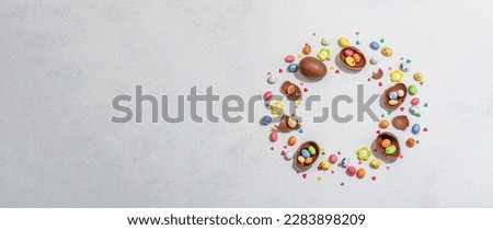 Traditional Easter sweets with eggs, chocolate rabbit, festive edible decor. Wreath with place for text, light stone background, flat lay, top view, banner format