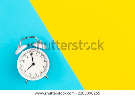 White alarm clock on a blue and yellow background, flat lay.