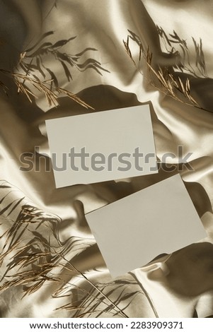 Blank paper sheet cards with mockup copy space, dried grass, soft sunlight shadows on glossy gold silk cloth. Aesthetic flat lay, top view minimal business brand template
