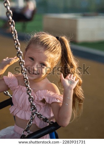 little girl in a pink dress swings on a swing happy