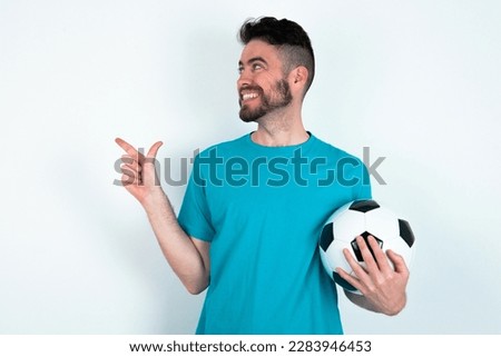 Optimistic young handsome man wearing blue T-shirt over white background points with both hands and  looking at empty space.