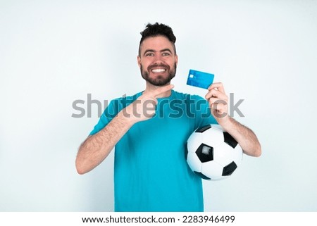 Photo portrait of young handsome man wearing blue T-shirt over white background doing purchase with pointing finger credit bank card