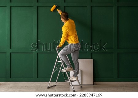 Young man with roller and ladder painting green wall