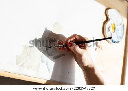 Young woman painting a picture with watercolor at wooden table, aquarelle process, girl sitting at the table and create picture