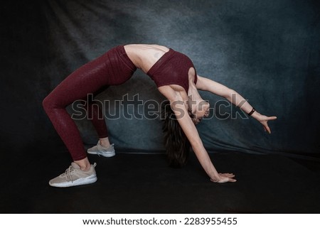 Caucasian slim girl in red sportswear make morning stretching exercises at blackstudio background. Fitness as active lifestyle