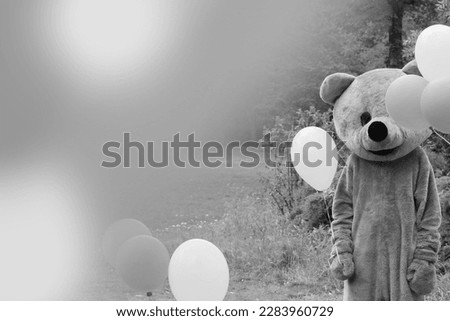 Man dressed as a teddy bear stands in a park surrounded by balloons. Black and white picture