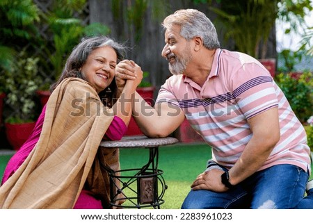 Happy senior couple play arm wrestling outdoors.