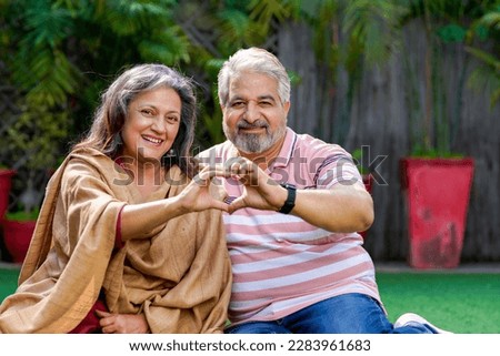 Indian senior couple smiling and making heart shape with hand.