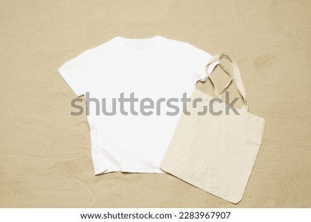 Mockup white not wrinkled summer t-shirt shopper copy space. Sand beach texture background. Blank template woman man shirt Top view. Summertime accessories. Flat-lay closeup tshirt. Beachtime