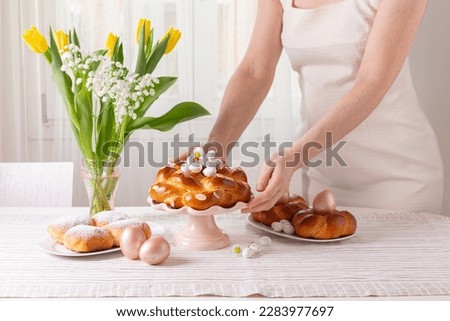 Woman preparing table with Easter pastry, eggs, candies and spring flowers for holiday. Happy Easter!  Light background.