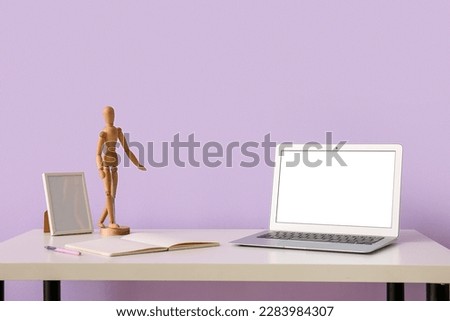 Workplace with laptop, mannequin and frame near lilac wall
