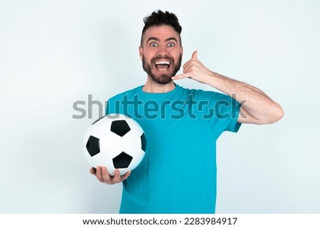 young handsome man wearing blue T-shirt over white background makes phone gesture, says call me back again, has glad expression.