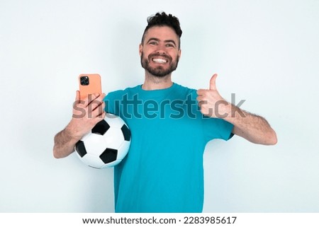 Portrait of young handsome man wearing blue T-shirt over white background using and texting with smartphone  happy with big smile doing ok sign, thumb up with fingers, excellent sign