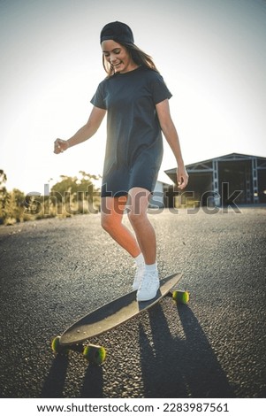 A pretty young woman with dark hair skateboarding in a vibrant urban environment. She is dressed in hip and trendy clothing and is captured in the stunning afternoon light.