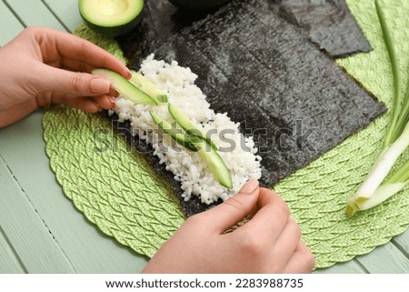 Woman preparing sushi rolls on green wooden background, closeup
