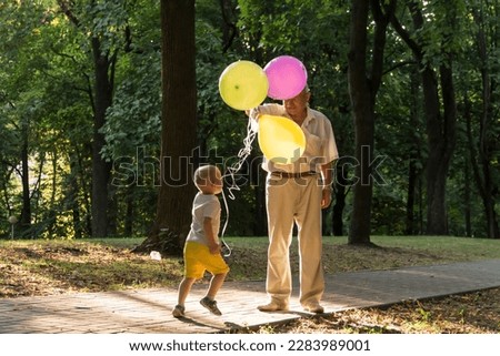 A little boy in yellow shorts and an elderly old man are playing with bright balloons. The family is having fun in the park in the fresh air and celebrating the holiday.