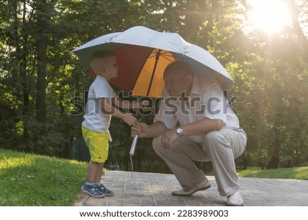 Grandson and grandfather to move out in the park under a bright umbrella at sunset. A pensioner and a little boy spend their free time on weekends together.