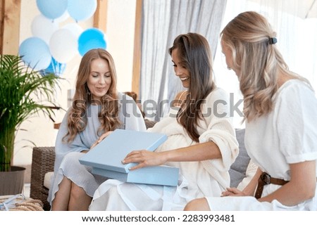 Caucasian pregnant woman opening gifts from friends at baby shower