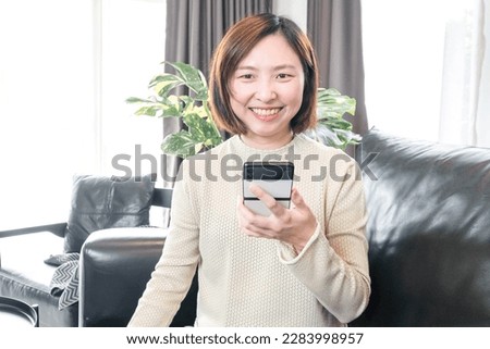 Happy relaxed young woman sitting on the sofa using a mobile phone Smiling woman laughing holding a smartphone looking at mobile phones enjoying online e-commerce shopping in mobile apps or watching v