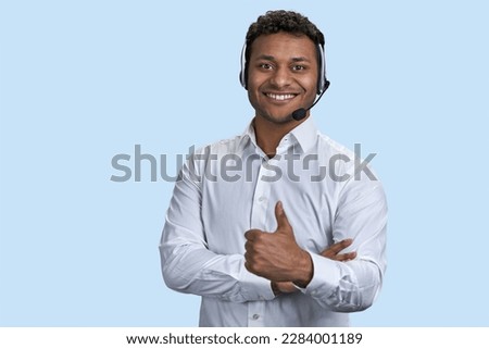 Portrait of a young smiling customer support worker. Indian man with headset. Pale blue background. Royalty-Free Stock Photo #2284001189