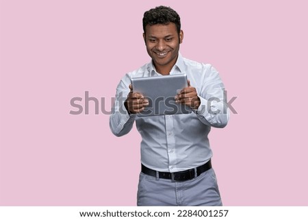 Portrait of a young indian businessman holding tablet pc. Isolated on pink background.