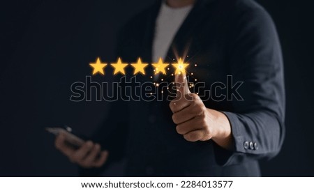 A satisfied customer gives a thumbs up for a five-star rating on his mobile phone, showing his positive feedback. Royalty-Free Stock Photo #2284013577
