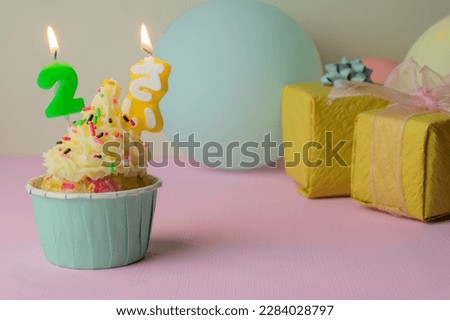 A birthday cupcake with buttercream frosting and chocolate sprinkes on pink background. (Text translation: 2 years old)