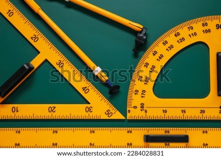 Protractor, triangle, ruler and compass on green chalkboard, flat lay