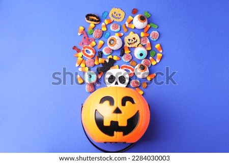 Halloween trick or treat bucket and different sweets on blue background, flat lay