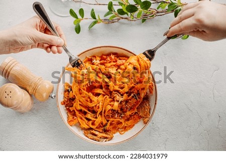Italian pasta, tomato sauce. Two female hands in the frame, girls eat pasta, hold forks in their hands, top view, Italian cuisine. Royalty-Free Stock Photo #2284031979
