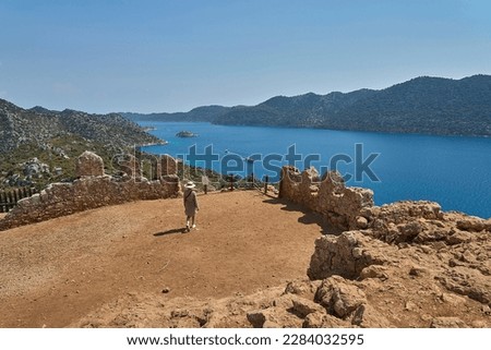 Tourist girl with hat walking and watching beautiful landscape panorama of Mediterranean Sea and Kekova islands from Castle of Simena (aka Kaleköy). Located between Kaş and Demre, Antalya, Turkey.