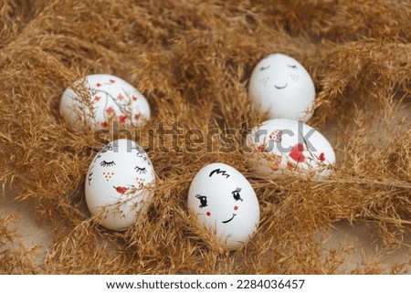 Easter card. Hand made Easter eggs lie in dry natural pampas grass. Painted gentle faces and red hearts. Dry golden reed. Soft selective focus. Happy holidays. Minimalist style. Copy Space