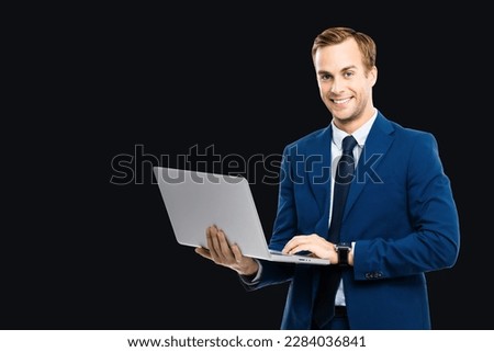 Photo of happy smiling businessman working with laptop, isolated on black background. Business man in blue confident suit and tie, with notebook in studio concept. 