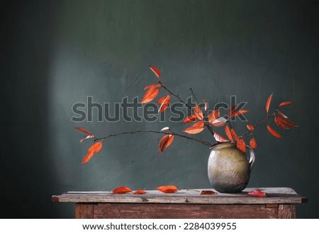 red autumn leaves in ceramic jug on old wooden table