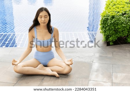 Summer woman practicing yoga in bikini fitness outfit by swimming pool in tropical resort and spa environment