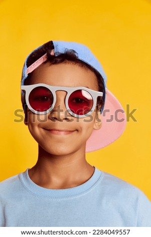 Closeup portrait of little african happy boy in stylish sunglasses and cap looking at camera over bright yellow background. Concept of music, happiness, kids emotions and ad Royalty-Free Stock Photo #2284049557