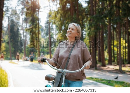 Senior older elderly modern woman rides a bicycle in a city park in the forest. Active pensioner, health lifestyle