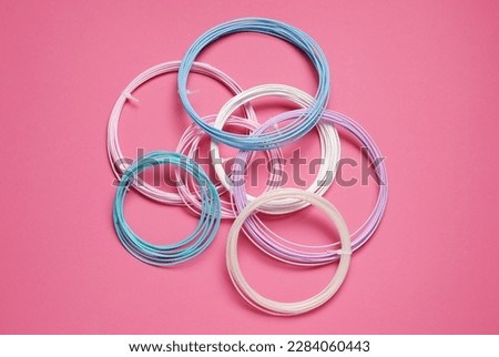 Colorful plastic filaments for 3D pen on pink background, flat lay
