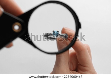 Jeweler examining topaz ring with magnifying glass on white background, closeup