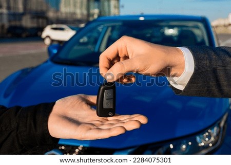 An employee of a dealership gives the key to a new car to a man on the background of a car outside Royalty-Free Stock Photo #2284075301