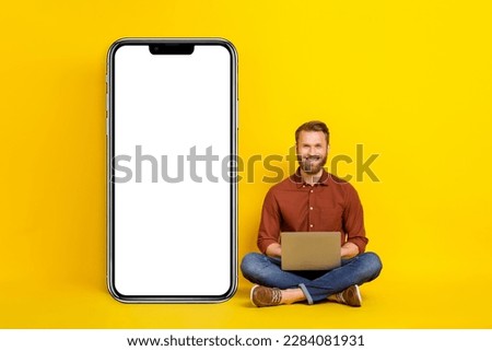 Full size photo of handsome guy sit floor use netbook empty space telephone display isolated on yellow color background