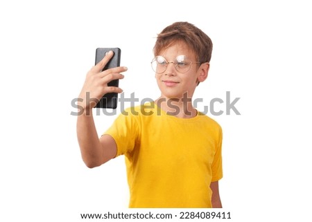Young teenager in glasses and a yellow t-shirt taking a selfie. Half-length studio portrait, isolated on a white background