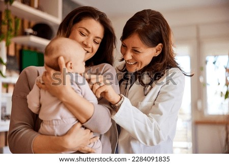 A smiling woman doctor pediatrician cuddles a cute baby girl on her cheek while her mother holding her. Royalty-Free Stock Photo #2284091835